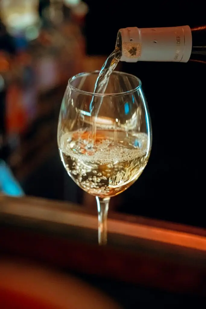 A close-up shot of white wine being poured into a glass in a cozy pub setting.