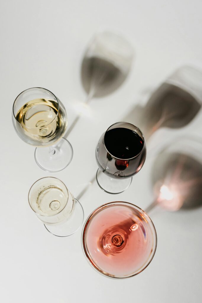 Aerial view of different wine glasses casting shadows on a white surface, showcasing a variety of wines.