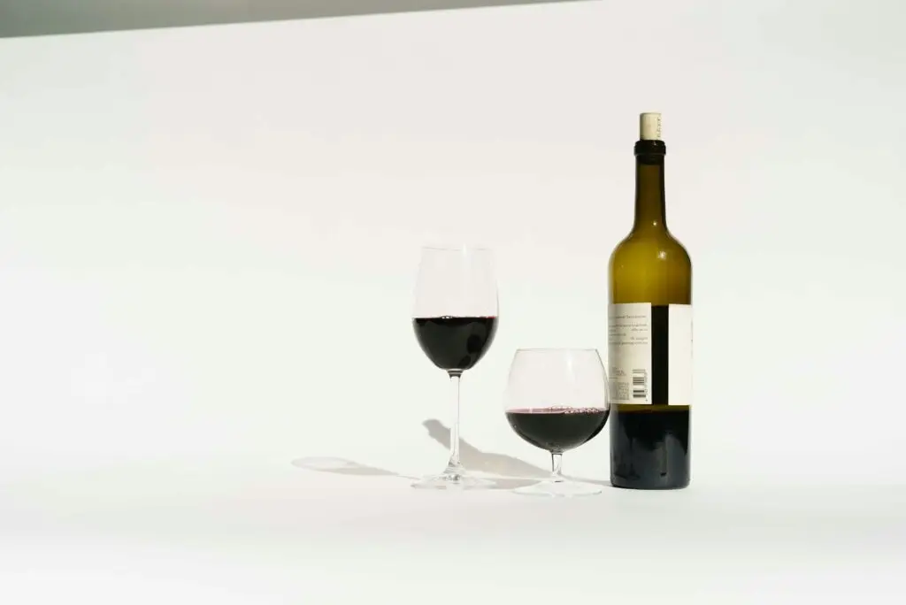 Red wine made from dark colored grape varieties in bottle and glasses placed in white studio