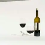 Red wine made from dark colored grape varieties in bottle and glasses placed in white studio